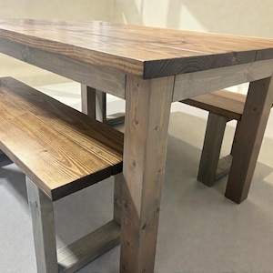 May include: A wooden dining table and bench set. The table has a rectangular top with a natural wood grain finish. The legs and bench frame are a lighter shade of wood. The bench is designed to fit under the table.