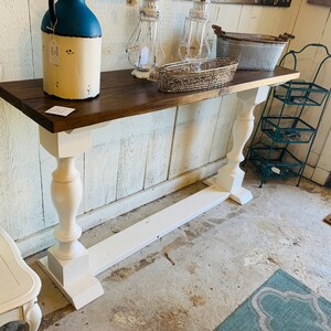 May include: A long, narrow console table featuring a dark brown rectangular wooden top supported by two white painted pedestal legs with a matching white horizontal base board connecting the feet at the bottom of the furniture piece.