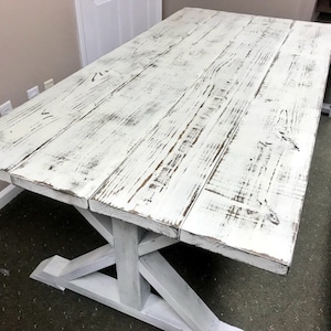 Weathered White Pedestal Farmhouse Table whith Distressed White Trestle Base and Weathered Top with Dark Walnut Showing Through Dining