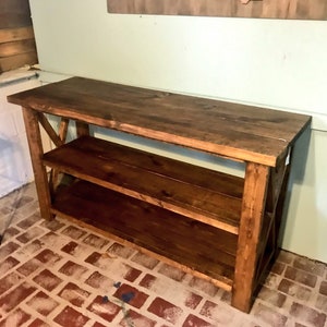 May include: A rectangular wooden console table with a dark brown stained finish. The piece features a flat top surface, one lower shelf, and side panels constructed with a visible X-shaped cross-brace design connecting the four vertical legs.