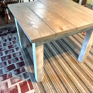 May include: A light gray wooden table with a distressed finish. The table has a rectangular top and four legs. The table is sitting on a striped rug.