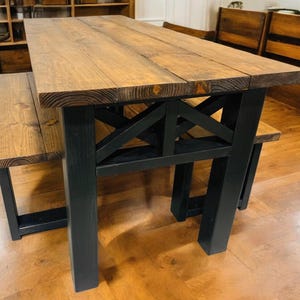May include: A wooden dining table with a black metal base and two matching benches. The table top is made of natural wood with a rustic finish. The benches have a simple design with a wooden seat and black metal legs.