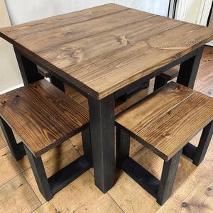 May include: A square dining table with a dark brown stained wood top and four thick black legs, accompanied by two matching rectangular benches with dark brown wood seats and black legs, arranged to fit neatly underneath the table surface.
