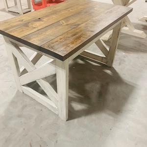May include: A rectangular table featuring a dark brown stained wooden top with visible grain patterns. The base consists of four white legs connected by cross-braced supports, showcasing a distressed finish with visible wood texture throughout.