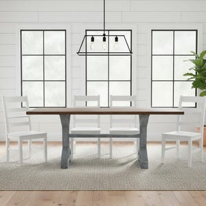 May include: A rectangular dining table with a dark brown wooden top and a gray trestle base, accompanied by four white ladder-back chairs. The furniture is arranged on a textured gray area rug in a room with white shiplap walls and windows.
