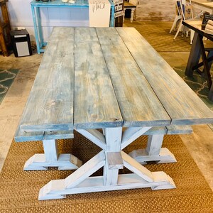 May include: A large, rectangular farmhouse-style table with a distressed blue-gray top and white, X-shaped legs. The table is made of wood and appears to be sturdy. The table is approximately 96 inches long.