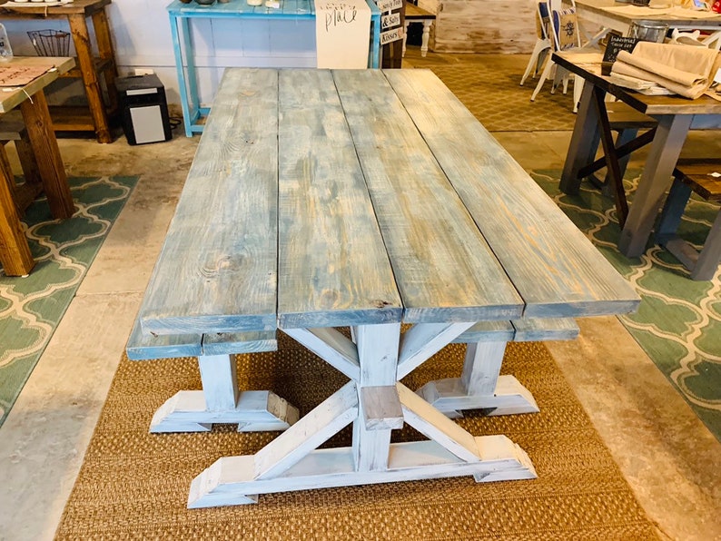 May include: A large, rectangular farmhouse-style table with a distressed blue-gray top and white, X-shaped legs. The table is made of wood and appears to be sturdy. The table is approximately 96 inches long.