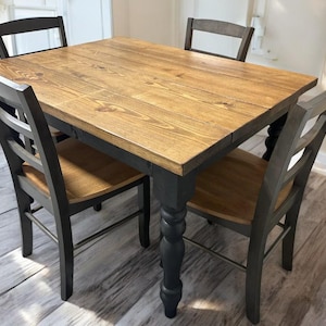 May include: A rectangular dining table with a natural wood grain top and four black turned legs, accompanied by four matching chairs featuring black ladder-back frames and natural wood seats, arranged around the table in a standard dining set configuration.