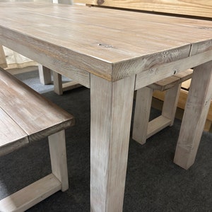 K&ouml;nnte beinhalten: Ein wei&szlig; gestrichener Holz-Esstisch mit zwei passenden B&auml;nken. Der Tisch hat eine rechteckige Tischplatte und dicke, quadratische Beine. Die B&auml;nke haben ein schlichtes Design mit einer rechteckigen Sitzfl&auml;che und zwei Beinen.