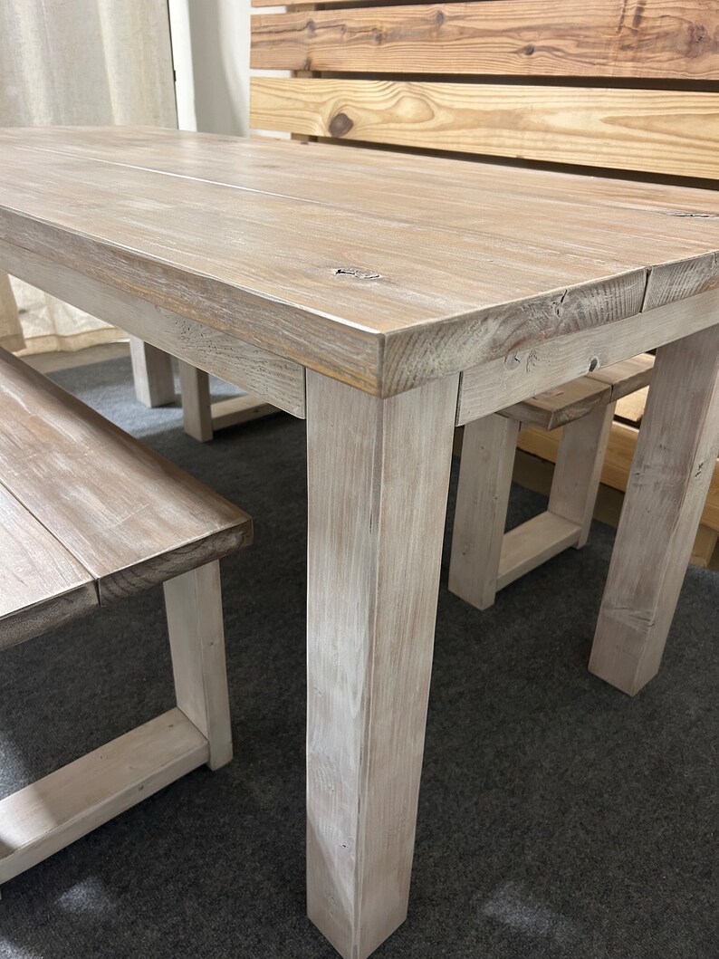K&ouml;nnte beinhalten: Ein wei&szlig; gestrichener Holz-Esstisch mit zwei passenden B&auml;nken. Der Tisch hat eine rechteckige Tischplatte und dicke, quadratische Beine. Die B&auml;nke haben ein schlichtes Design mit einer rechteckigen Sitzfl&auml;che und zwei Beinen.