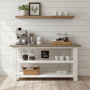 May include: A white wooden console table with a gray top featuring two open shelves. The surface holds an espresso machine, a coffee grinder, a white canister labeled COFFEE, and a wooden tray with glass jars. A sign reads Rise & Grind.