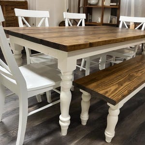 May include: A rectangular dining table with a dark brown stained wood top and white painted legs, accompanied by three white chairs with cross-back designs and a matching rectangular bench with a dark brown wood top and white turned legs.
