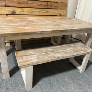 K&ouml;nnte beinhalten: Esstisch und Bank aus wei&szlig; gebleichtem Holz. Der Tisch hat eine rechteckige Platte und vier Beine. Die Bank hat eine rechteckige Platte und zwei Beine an jedem Ende.