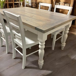 May include: A farmhouse style dining table with a gray washed wood top and white painted legs. The table has four white chairs with a ladder back design.