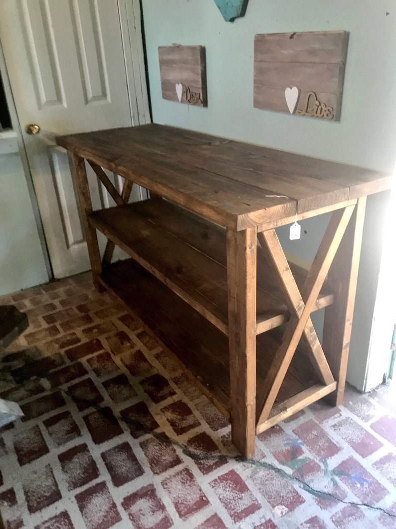 May include: A rectangular wooden console table with a dark brown stained finish. The piece features a flat top surface, a lower shelf, and side panels constructed with a prominent X-shaped support brace design. The table stands on four legs.