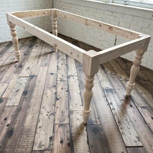 May include: Unfinished wooden table frame with turned legs. The rectangular frame is constructed from light-colored wood, showcasing the natural grain. The turned legs add a classic touch to the design. The table frame is ready for finishing and assembly.