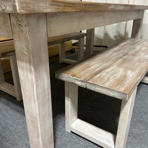 K&ouml;nnte beinhalten: Ein wei&szlig; gestrichener Holz-Bauerntisch mit zwei passenden B&auml;nken. Der Tisch hat eine dicke, rechteckige Tischplatte und stabile Beine. Die B&auml;nke haben ein schlichtes, rechteckiges Design.