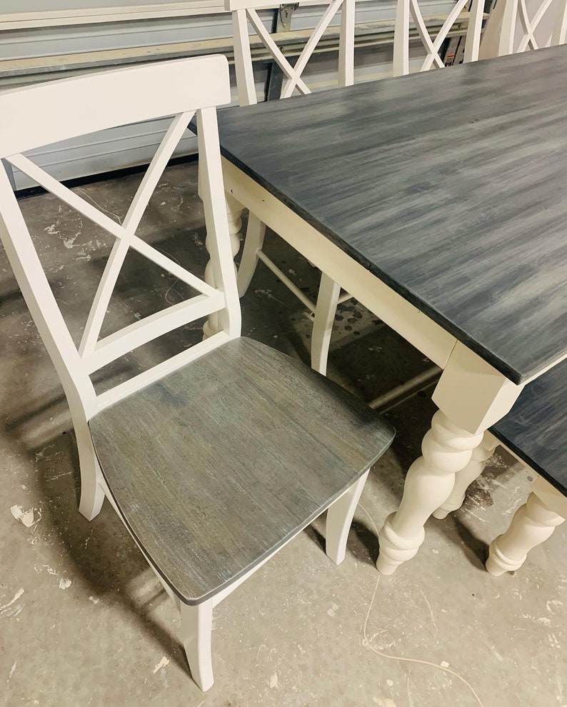 K&ouml;nnte beinhalten: Ein Esszimmerset bestehend aus einem rechteckigen Tisch und St&uuml;hlen mit wei&szlig;en Rahmen sowie dunkelgrau gebeizten Holzsitzen und Tischplatten. Die St&uuml;hle haben ein X-f&ouml;rmiges R&uuml;ckendesign und gedrechselte Beine im Spindelstil.
