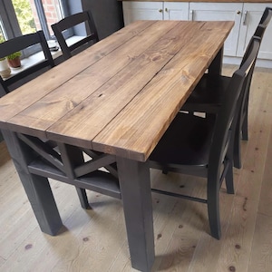 May include: A wooden dining table with a natural finish, paired with four dark gray chairs. The table has a rectangular top and a cross-braced base. The chairs have a simple, classic design. The table is approximately 60 inches long.