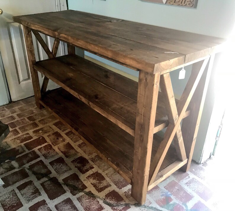 May include: A rectangular wooden console table with a dark brown stained finish. The piece features a flat top surface, one lower shelf, and sturdy legs connected by X-shaped cross-bracing on both sides, providing a stable and open structure.