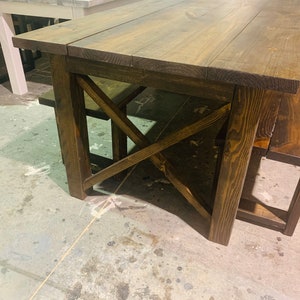 May include: A rustic wooden dining table and bench set. The table features a dark brown stained finish with a planked top and an X-shaped support. The matching bench is also stained dark brown.