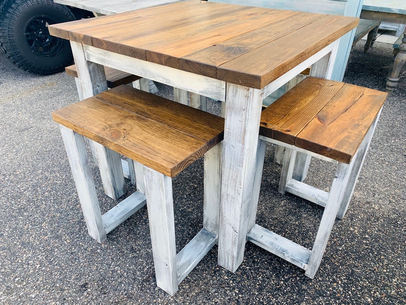 K&ouml;nnte beinhalten: Ein quadratischer Holztisch mit dunkelbraun gebeizter Platte und einem wei&szlig; gestrichenen Gestell im Used-Look, dazu zwei passende B&auml;nke mit dunkelbraun gebeizten Sitzfl&auml;chen und wei&szlig; gestrichenen Beinen im Used-Look, alle mit stabilem Rahmen.