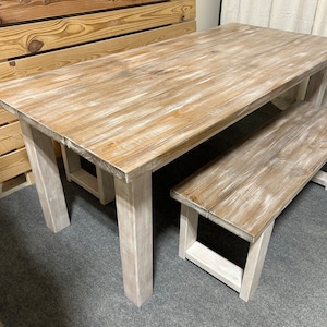 K&ouml;nnte beinhalten: Ein wei&szlig; get&uuml;nchter Holz-Esstisch mit einer passenden Bank. Der Tisch hat eine rechteckige Tischplatte und vier Beine. Die Bank hat eine rechteckige Tischplatte und zwei Beine an jedem Ende.