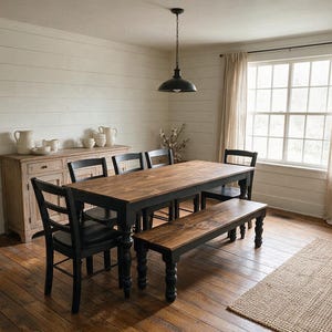 May include: A rectangular dining table with a natural wood top and black legs, accompanied by three black chairs and a matching wooden bench. The set is positioned on a wooden floor in a room with white horizontal wall paneling and a window.