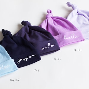 Peut inclure: Cinq bonnets pour b&eacute;b&eacute; personnalis&eacute;s dans diff&eacute;rentes couleurs&nbsp;: bleu ciel, marine, denim, orchid&eacute;e et lavande. Les bonnets sont en coton doux et ont un n&oelig;ud sur le dessus. Chaque bonnet est brod&eacute; d&rsquo;un nom diff&eacute;rent&nbsp;: Rea, Jasper, Arlo, Bella et Harper.