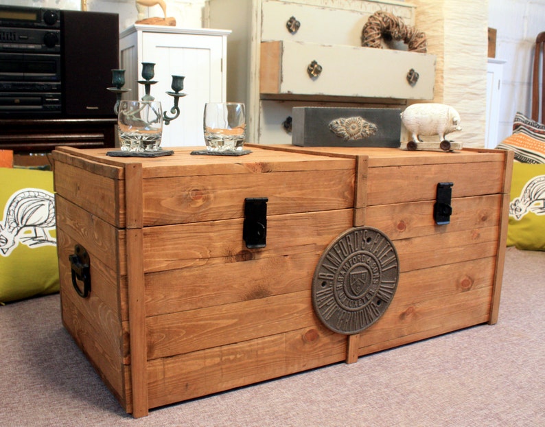 wooden chest resting on the floor, made of rustic reclaimed solid wood, with two black hasp and staples and a large round plaque.