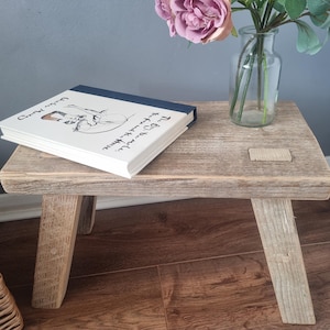 May include: A rustic wooden stool with a weathered gray finish. The stool has three legs and a rectangular top. A book titled "The Boy, the Mole, the Fox and the Horse" is resting on the top of the stool.