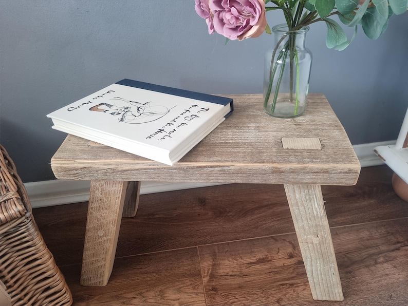 May include: A rustic wooden stool with a weathered gray finish. The stool has three legs and a rectangular top. A book titled "The Boy, the Mole, the Fox and the Horse" is resting on the top of the stool.