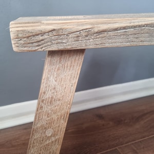May include: A rustic wooden bench with a natural, weathered finish. The bench has a simple design with two angled legs and a rectangular top.