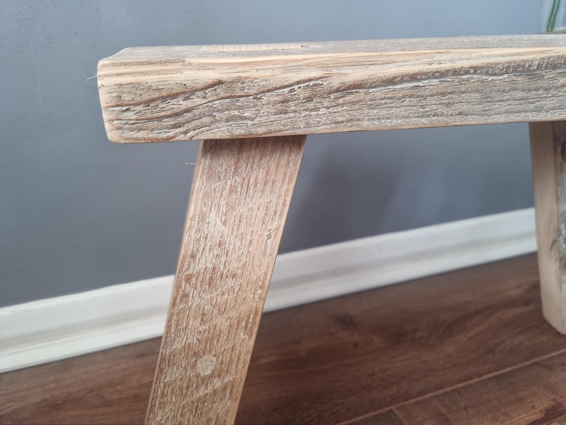 May include: A rustic wooden bench with a natural, weathered finish. The bench has a simple design with two angled legs and a rectangular top.