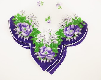 May include: A white cotton handkerchief with a purple and green floral design. The handkerchief has a scalloped edge and is folded in half.