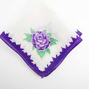 May include: A white handkerchief with a purple flower design and a purple border.