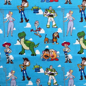 Op de afbeelding: Een herhalend patroon van Toy Story-personages op een lichtblauwe achtergrond. Het ontwerp bevat Woody, Buzz Lightyear, Jessie, Rex en andere personages uit de animatiefilm, met witte wolkenaccenten.