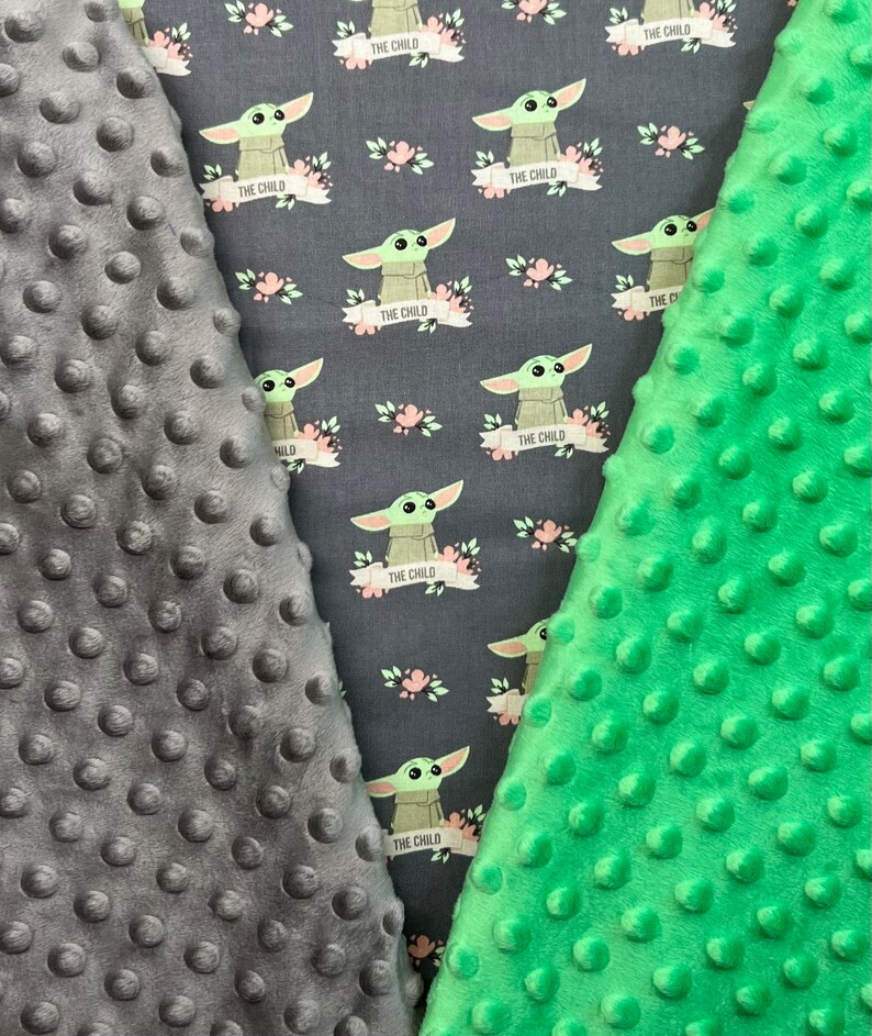 May include: Two pieces of fabric, one gray and one green, with a repeating pattern of a green alien character with the text "The Child" on a banner. Both fabrics have a textured, bumpy surface.