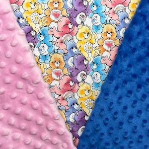 May include: A colorful fabric featuring a pattern of Care Bears in various colors, including pink, yellow, blue, and purple. The fabric is flanked by a pink, dimpled fabric on the left and a blue, dimpled fabric on the right. The Care Bears have hearts and other symbols.