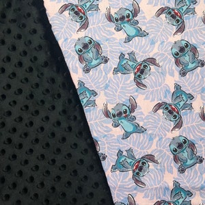 Pu&ograve; includere: Un tessuto nero e bianco con un motivo di personaggio dei cartoni animati blu. Il personaggio &egrave; Stitch di Lilo & Stitch. Il tessuto &egrave; morbido e peluche.