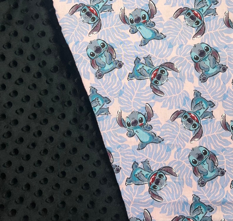 Pu&ograve; includere: Un tessuto nero e bianco con un motivo di personaggio dei cartoni animati blu. Il personaggio &egrave; Stitch di Lilo & Stitch. Il tessuto &egrave; morbido e peluche.