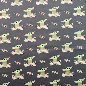 May include: A dark gray fabric with a repeating pattern of a green alien character with big eyes and the text "THE CHILD" on a white banner. The alien is surrounded by pink flowers.