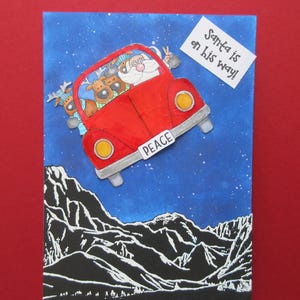 Kerstkaart, leuke kerstkaart, "De kerstman is onderweg", vliegend door de lucht over de bergen met zijn rendieren in een rode VW-kever.