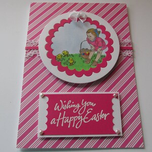 Tarjeta de Pascua, con una niña cuidando de las pequeñas chics, cesta de Pascua a su lado, "Deseándote una feliz Pascua"