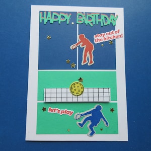 Tarjeta de cumpleaños de Pickleball: "Feliz cumpleaños, ¡no te acerques a la cocina!, ¡vamos a jugar!". Dos jugadores en la cancha, uno en la cocina.