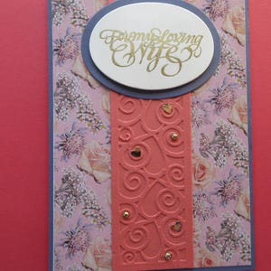 Tarjeta de aniversario con hermoso fondo de flores, "Para mi amada esposa", marco azul oscuro, con franja naranja oscura con corazones dorados.