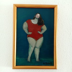Puede incluir: Una pintura enmarcada de una mujer en un traje de baño rojo de pie sobre un fondo azul verdoso. La mujer tiene el pelo largo y oscuro y está mirando al espectador. La pintura está firmada "M. Pardo B."
