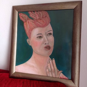Puede incluir: Una pintura enmarcada de una mujer con un peinado naranja brillante, vistiendo un vestido rosa claro, sobre un fondo azul verdoso. La mujer mira hacia arriba y hacia la derecha, con la boca abierta como si estuviera cantando. La pintura está firmada en la esquina inferior derecha.