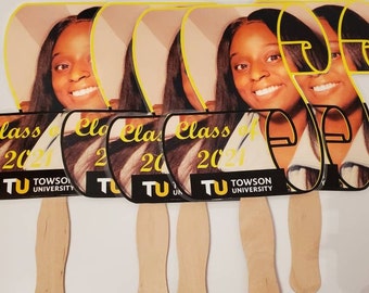 May include: Five yellow and black graduation fans with the text "Class of 2021" and "Towson University" printed on them. The fans feature a photo of a person wearing a graduation gown.