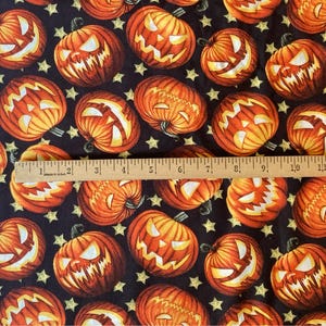 May include: Halloween-themed fabric featuring orange jack-o'-lanterns with glowing faces on a black background with yellow stars. A wooden ruler shows measurements up to 12 inches. The fabric is labeled "DAVID TEXTILES, INC."